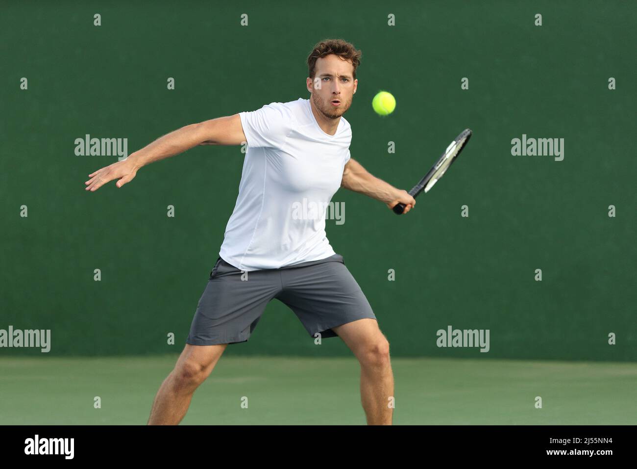 Tennis player man hitting ball with racket on green background. Sports athlete training forehand grip technique on outdoor court Stock Photo