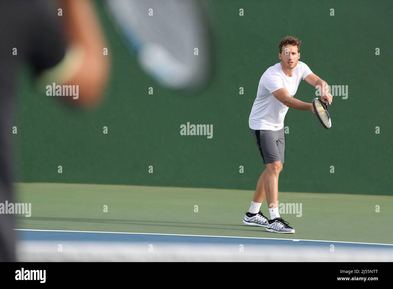 Tennis serve player man serving ball during match point on outdoor green court. Two men athlete playing sport game training doing exercise Stock Photo