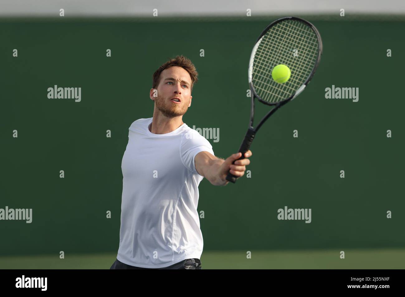 Tennis player man hitting ball playing tennis match on outdoor hard court in fitness club. Male sport athlete healthy lifestyle Stock Photo
