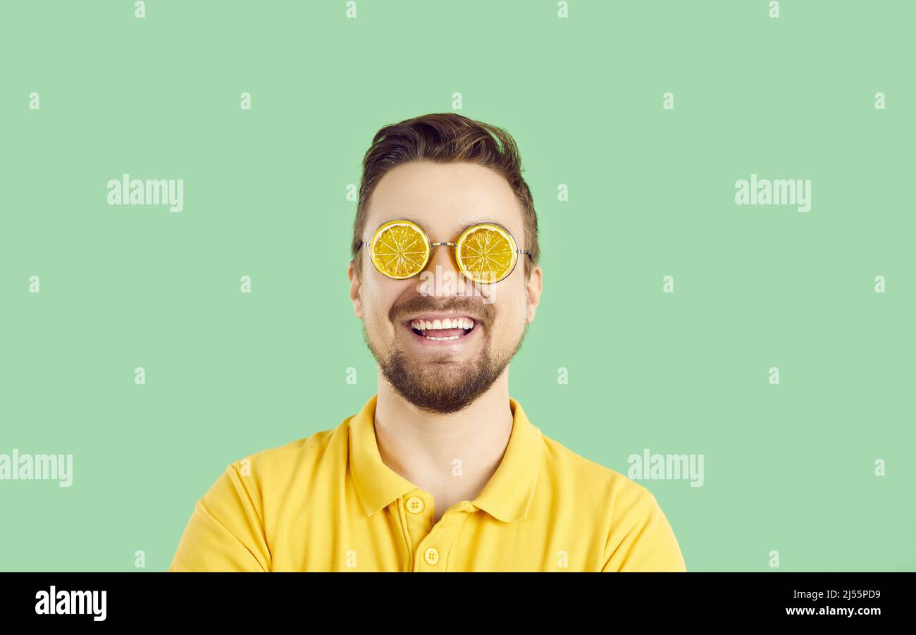 Cheerful positive man in summer glasses in shape of orange slices on light green background. Stock Photo