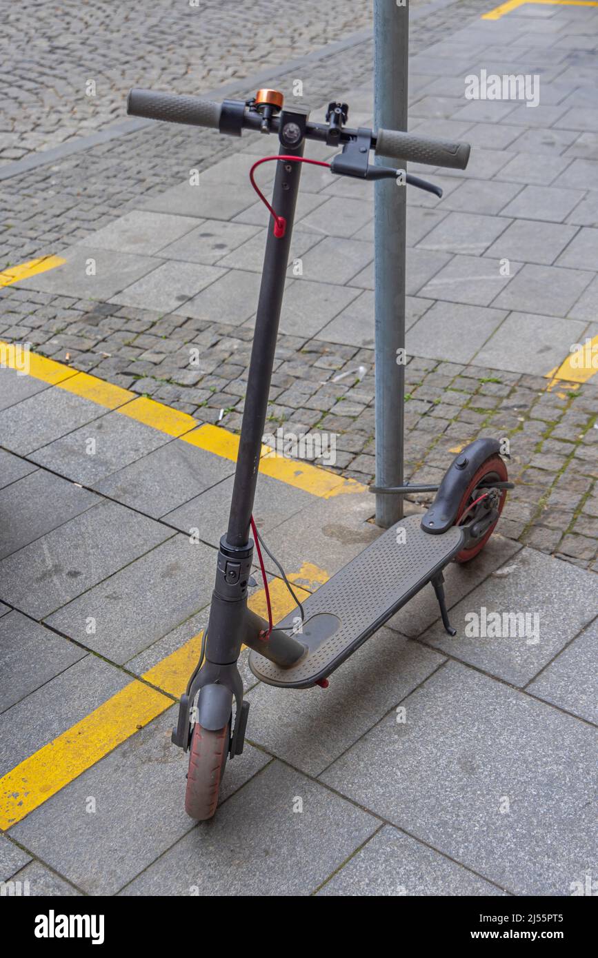 Electric Scooter Back Wheel Locked to Pole Parked at Street Stock Photo