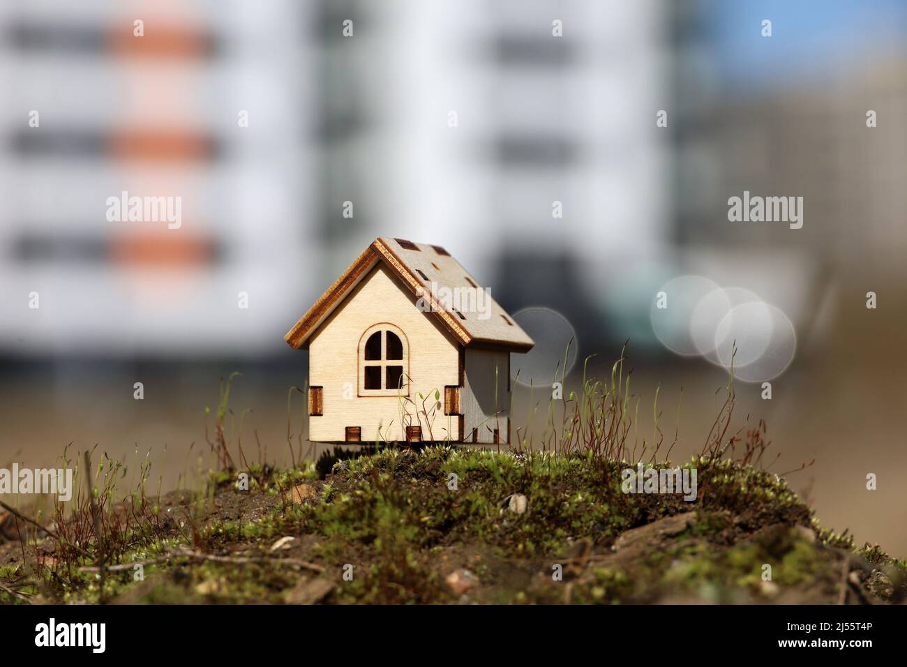 Wooden house model on background of high-rise residential buildings. Concept of country cottage, real estate in ecologically clean area Stock Photo