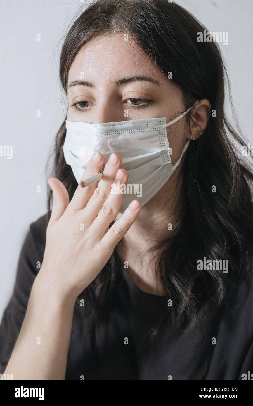 Senior woman hold a cigarette in mouth,withdrawal symptoms,cigarette cravings,feeling stressful while wear a face mask during the pandemic Covid-19,Co Stock Photo