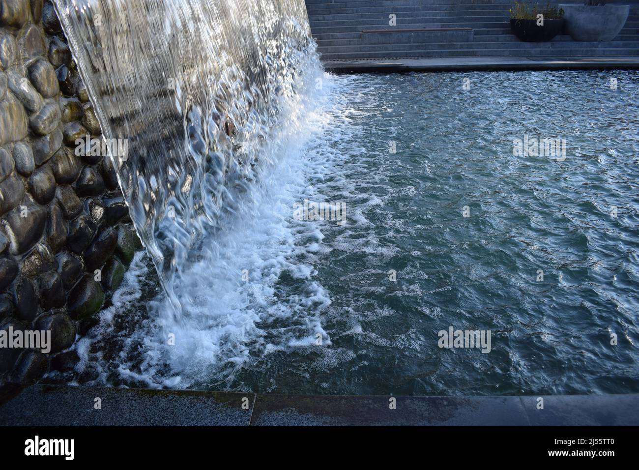 A waterfall flowing at park. A waterfall of a fountain in a garden. Wall of water. A beautiful view of the falling water cascade. Artificial waterfall Stock Photo