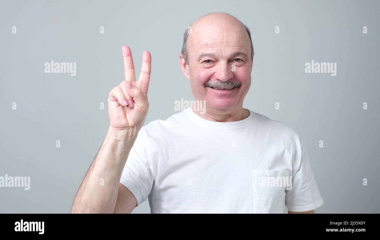 Senior man raising two fingers up on hand showing peace or victory symbol. Supporting anti war movement. Stock Photo
