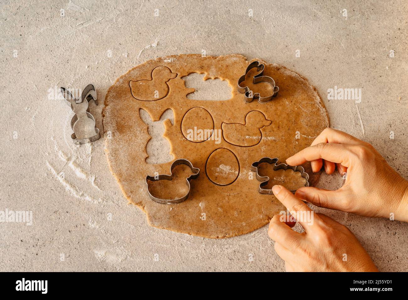 Process of making gingerbread biscuits on table full of flour.Woman hands preparing Easter cookies from honey dough.Easter bunny,rabbit,eggs and ducks Stock Photo