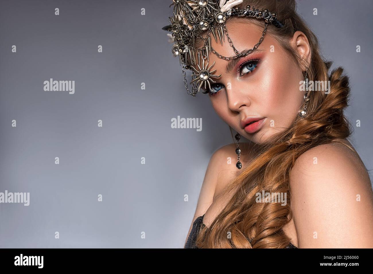 Close up portrait of a young beautiful blonde woman wearing a crown and costume jewelry on a gray background Stock Photo