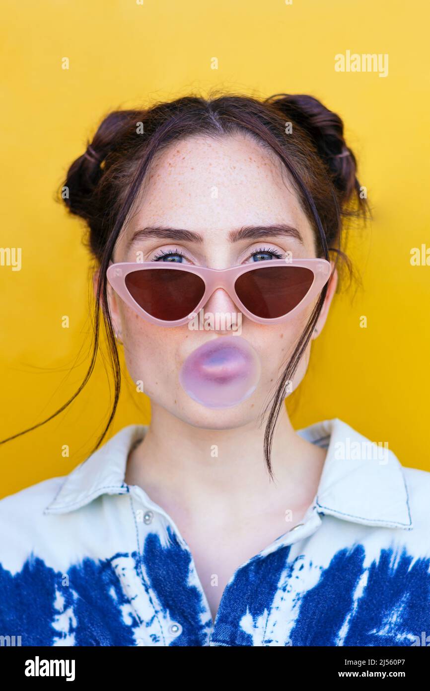 woman blowing a bubble gum bubble on a yellow background Stock Photo