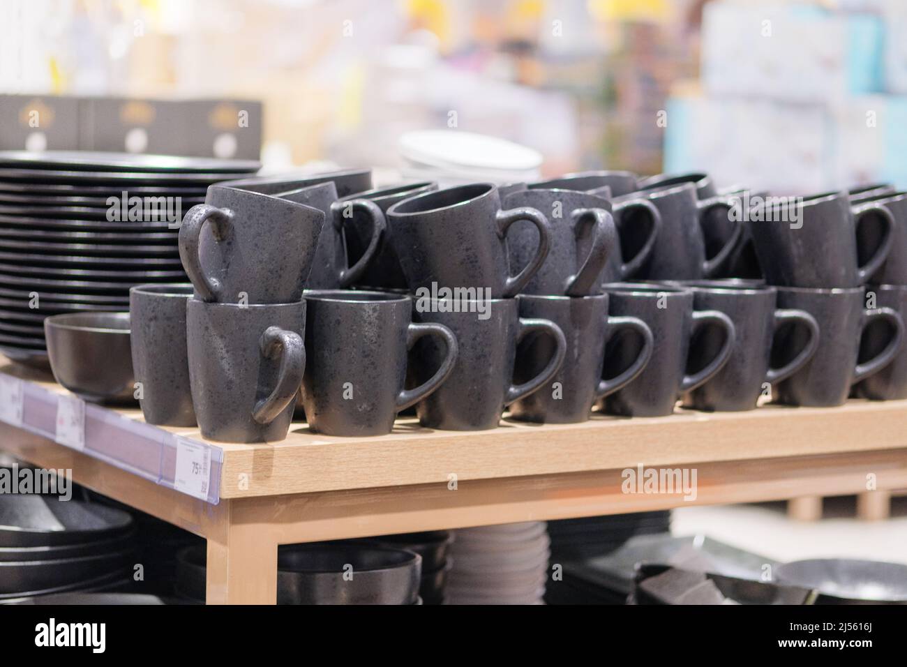 Сups are sold at the store. Rows of different black cups for home on shelves in a supermarket. Stock Photo