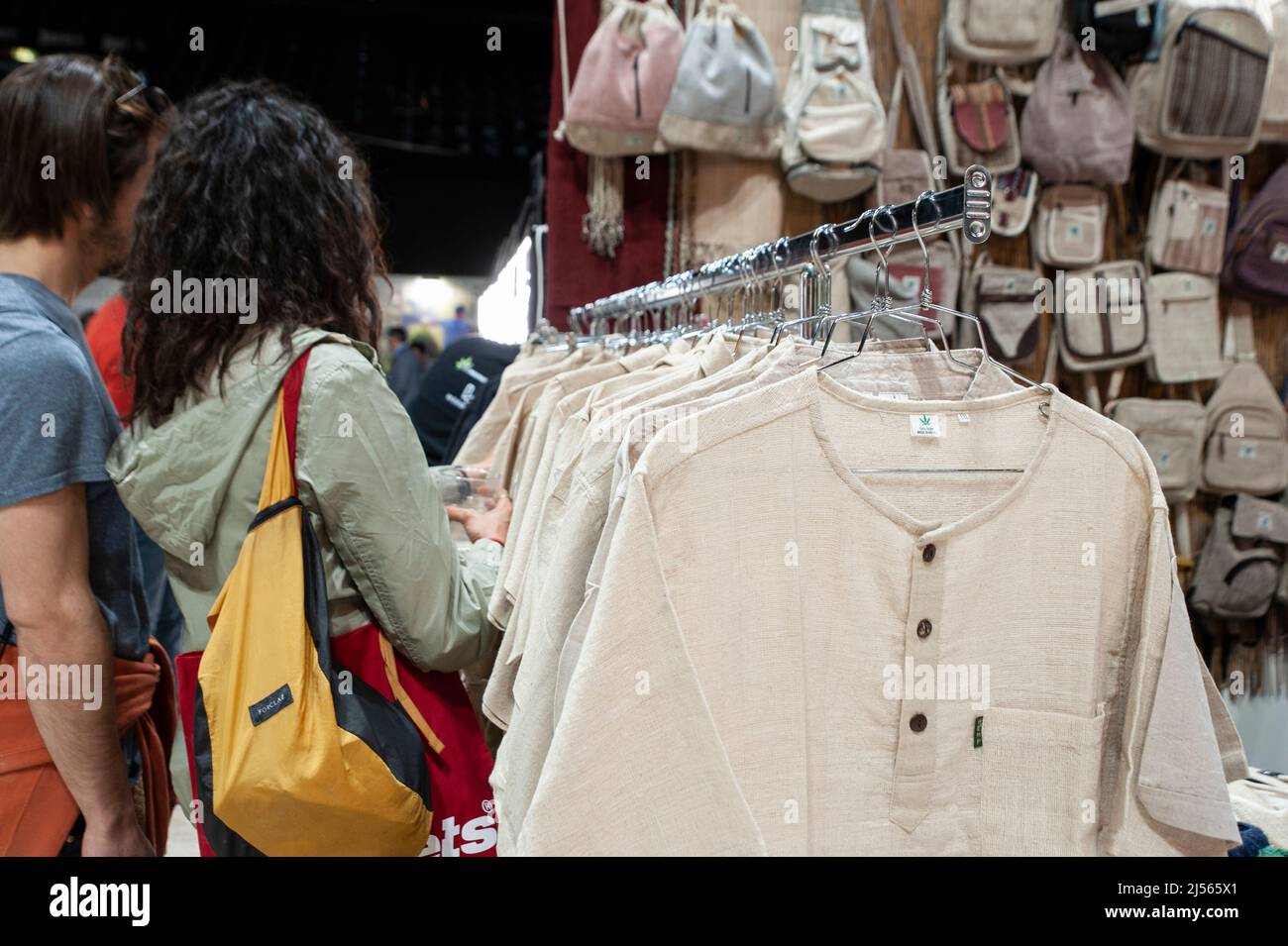 Visitors at the trade show “Indicasativa 2022” devoted to the hemp world. Shopping at the market stall. Canvas clothes in the foreground. Stock Photo