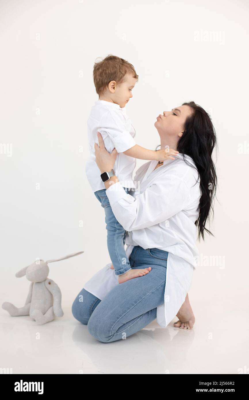 Vertical portrait of single mother, dark haired woman with little boy, her son, embracing together, kissing. Mother day Stock Photo