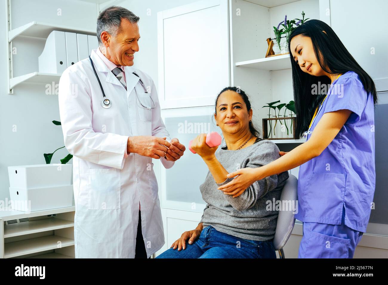 rehabilitation doctor physiotherapist physician and nurse practitioner helping patient lift dumbbell with one hand. Healthcare industry clinic Stock Photo