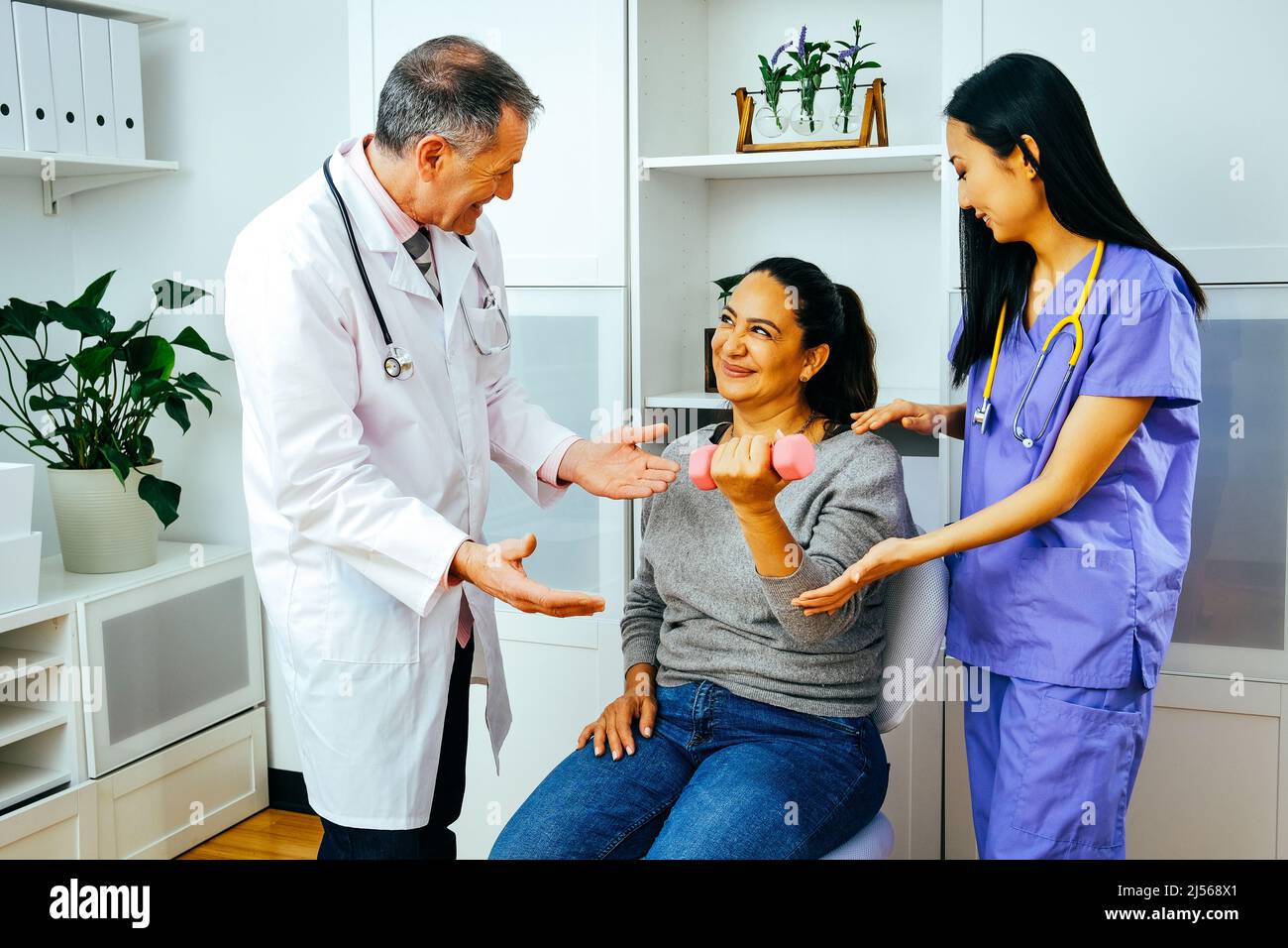smiling rehabilitation doctor physiotherapist physician and nurse practitioner helping patient lift dumbbell with one hand. Healthcare industry clinic Stock Photo