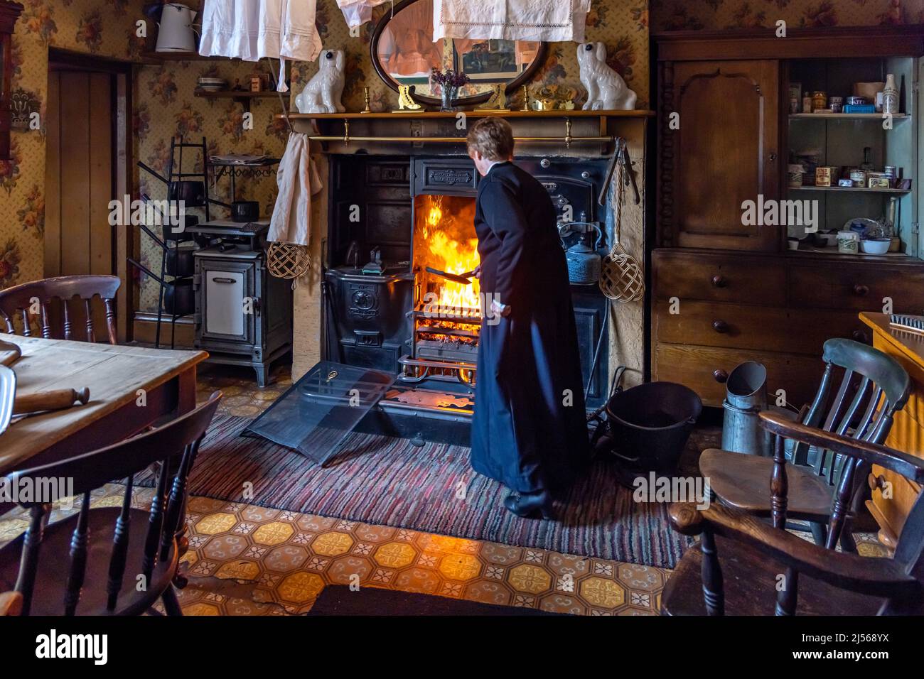 Woman in period dress tending fire in cottage at the Beamish Open Air Museum, near Stanley in County Durham Stock Photo