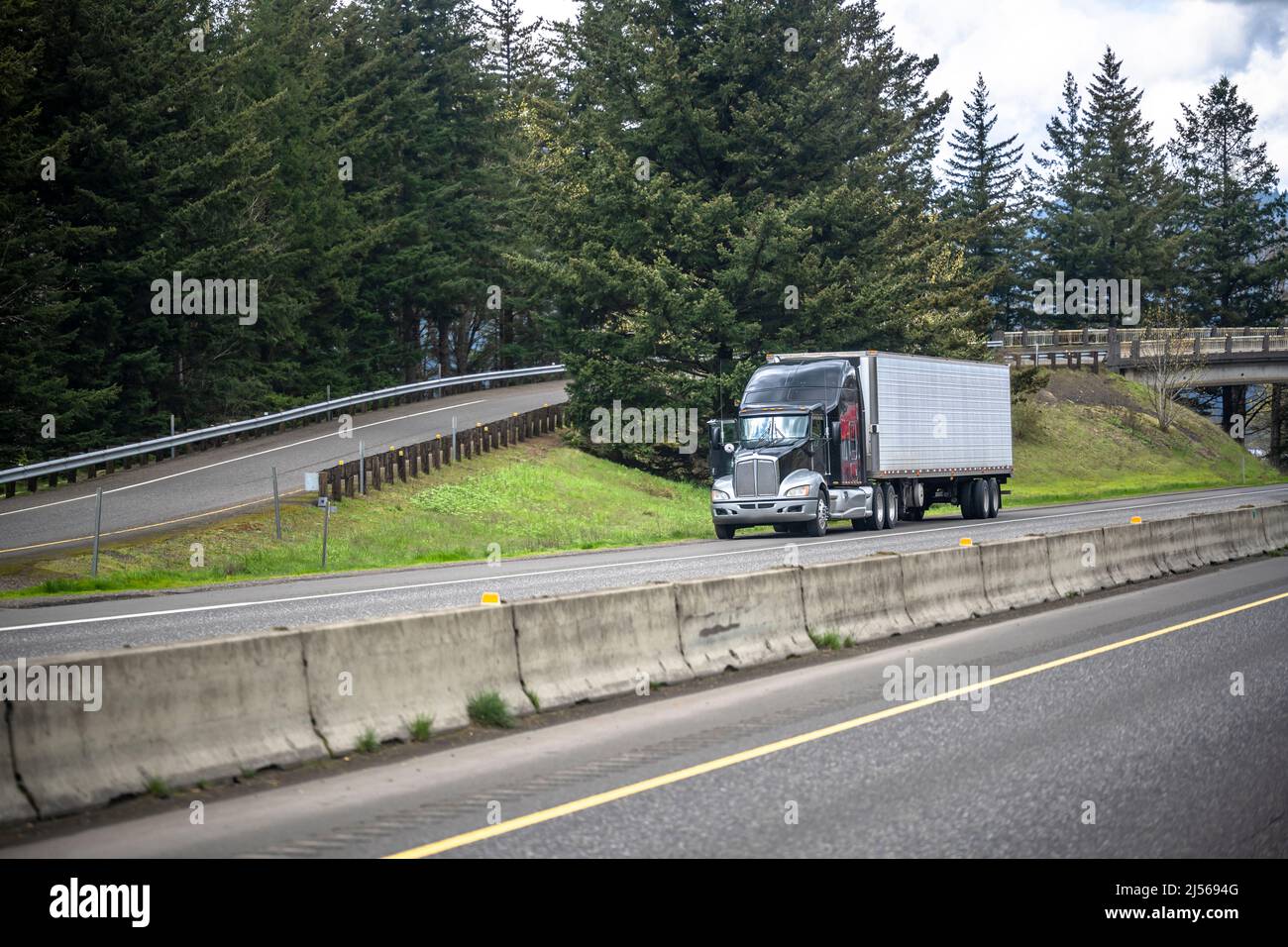 Popular industrial standard big rig black semi truck tractor with loaded refrigerator semi trailer standing  out of service on highway road shoulder w Stock Photo
