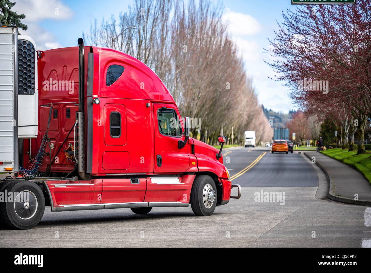 Industrial standard bright red high cab long haul big rig semi truck with reefer semi trailer transporting commercial cargo turning on the local city Stock Photo