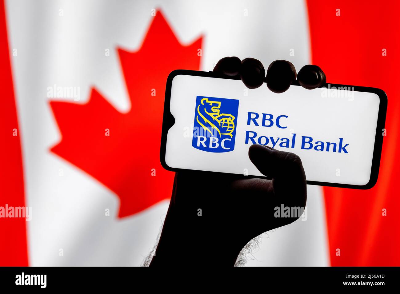 Smartphone with Royal Bank of Canada logo in clenched hand on background of Canadian flag Stock Photo