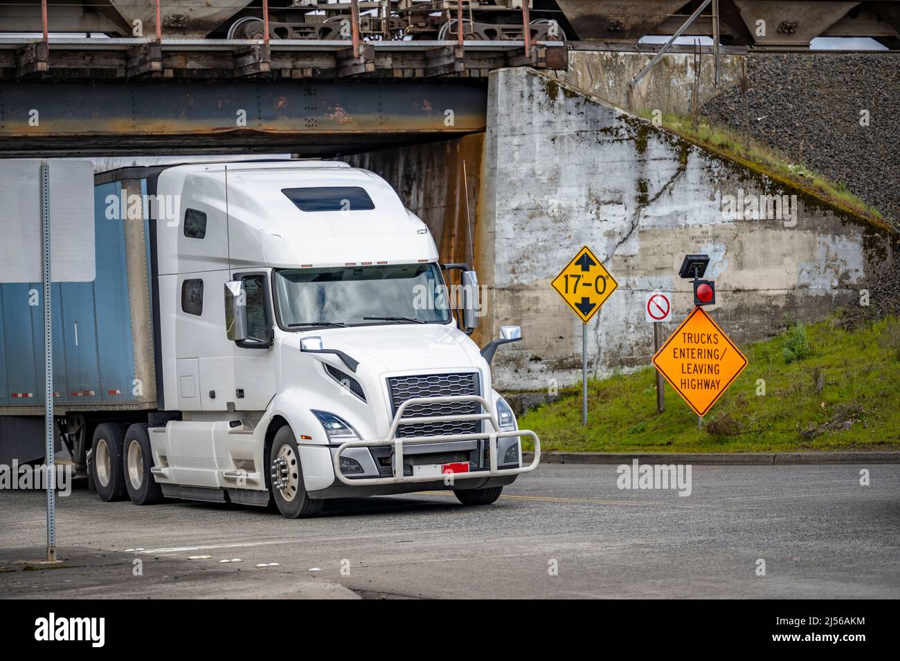 Industrial standard bright white high cab long haul big rig semi truck with dry van semi trailer transporting commercial cargo turning on the local ci Stock Photo