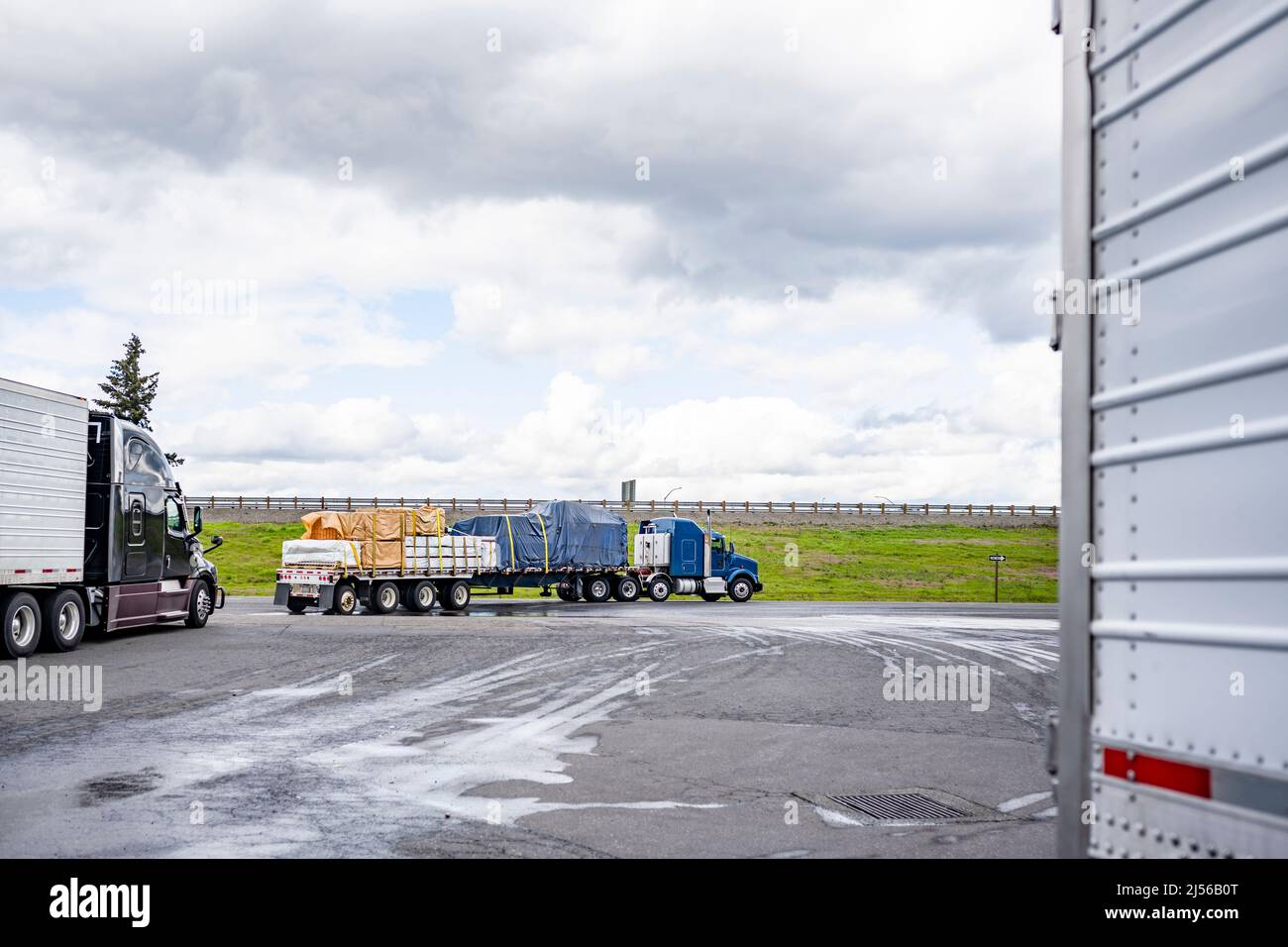 Industrial standard loaded big rig semi trucks with flat bed and refrigerator semi trailers going on truck stop exit running to highway entrance in Co Stock Photo