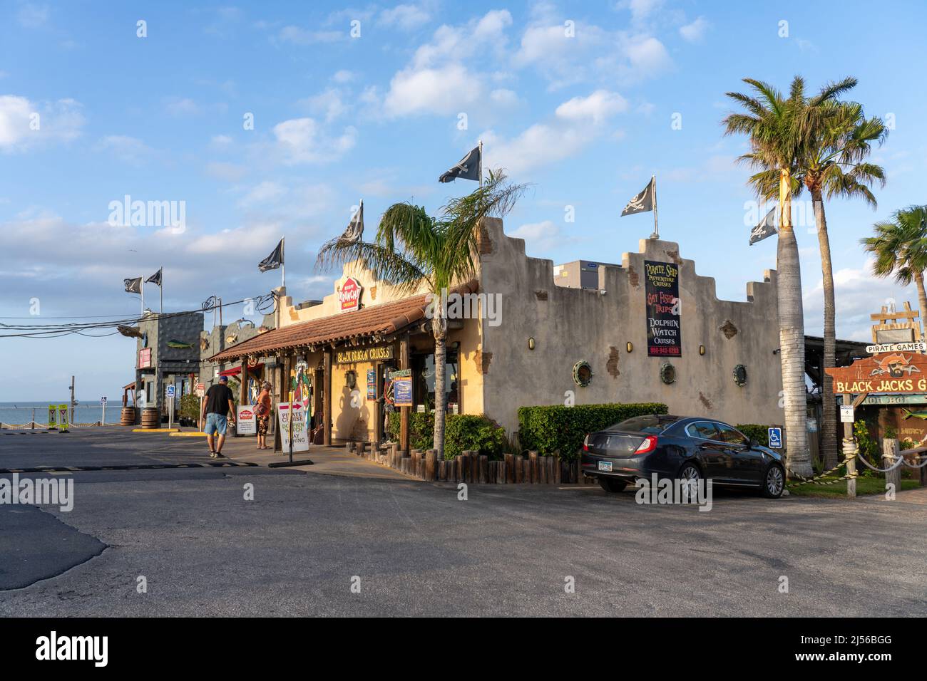 A tourist shop and boat tour office with pirate flags by the Laguna Madre in Port Isabel, Texas.  Two older tourists stand in front. Stock Photo