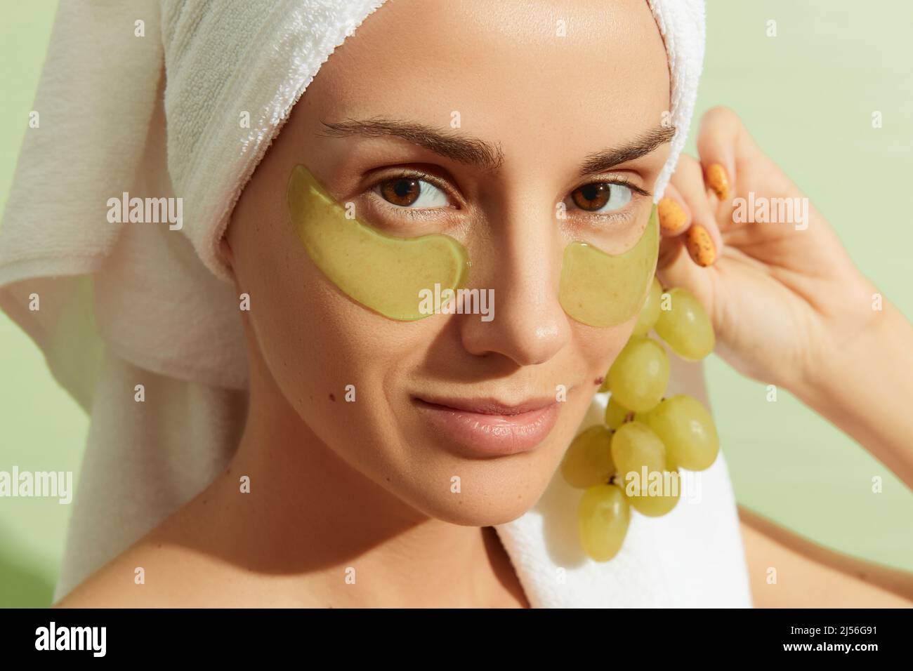 Woman using grapeseedbased eye patches on pastel green background