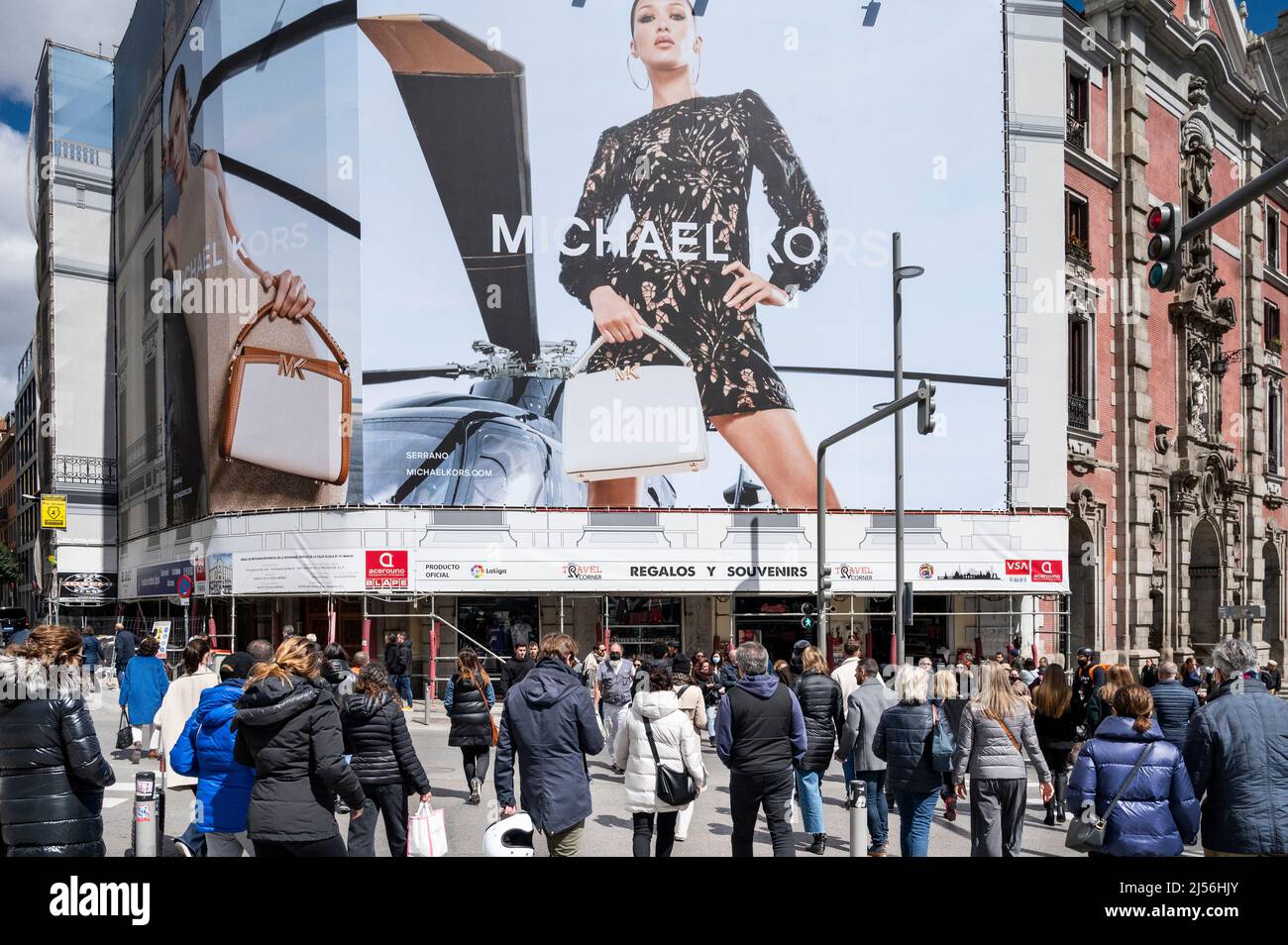 Pedestrians wait at a traffic light as a street commercial banner ad from the American clothing fashion brand Michael Kors MK is seen opposite side in Spain Stock Photo Alamy