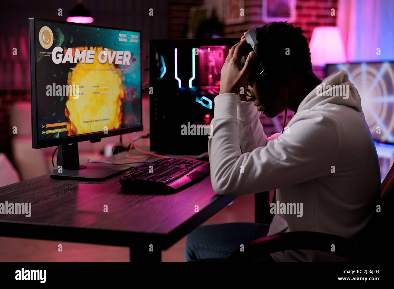 Frustrated young adult losing online video games play competition on computer with neon lights. Male gamer streaming action gameplay and feeling sad about lost shooting championship. Stock Photo