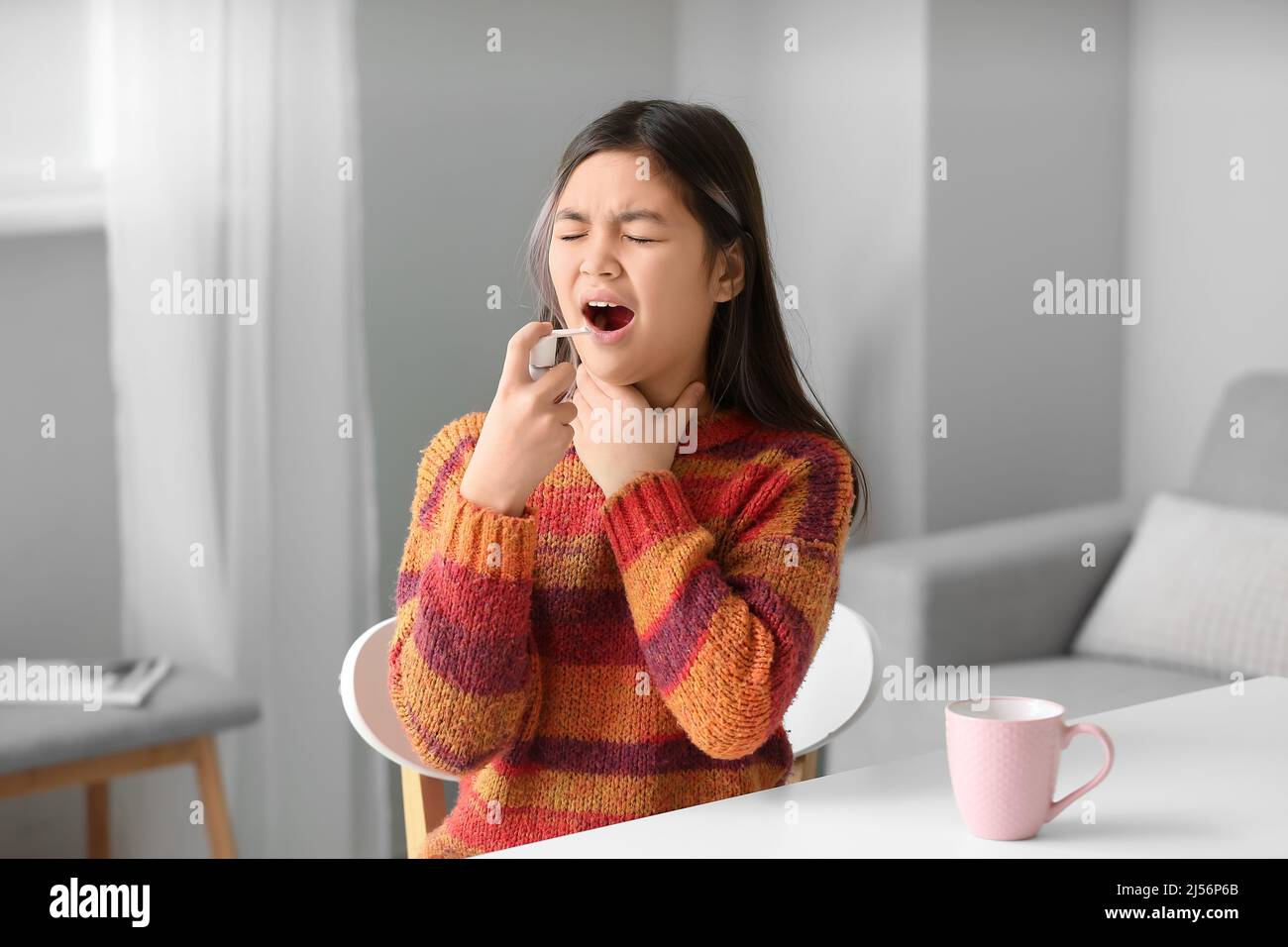 Ill Asian girl with sore throat using inhaler at home Stock Photo Alamy