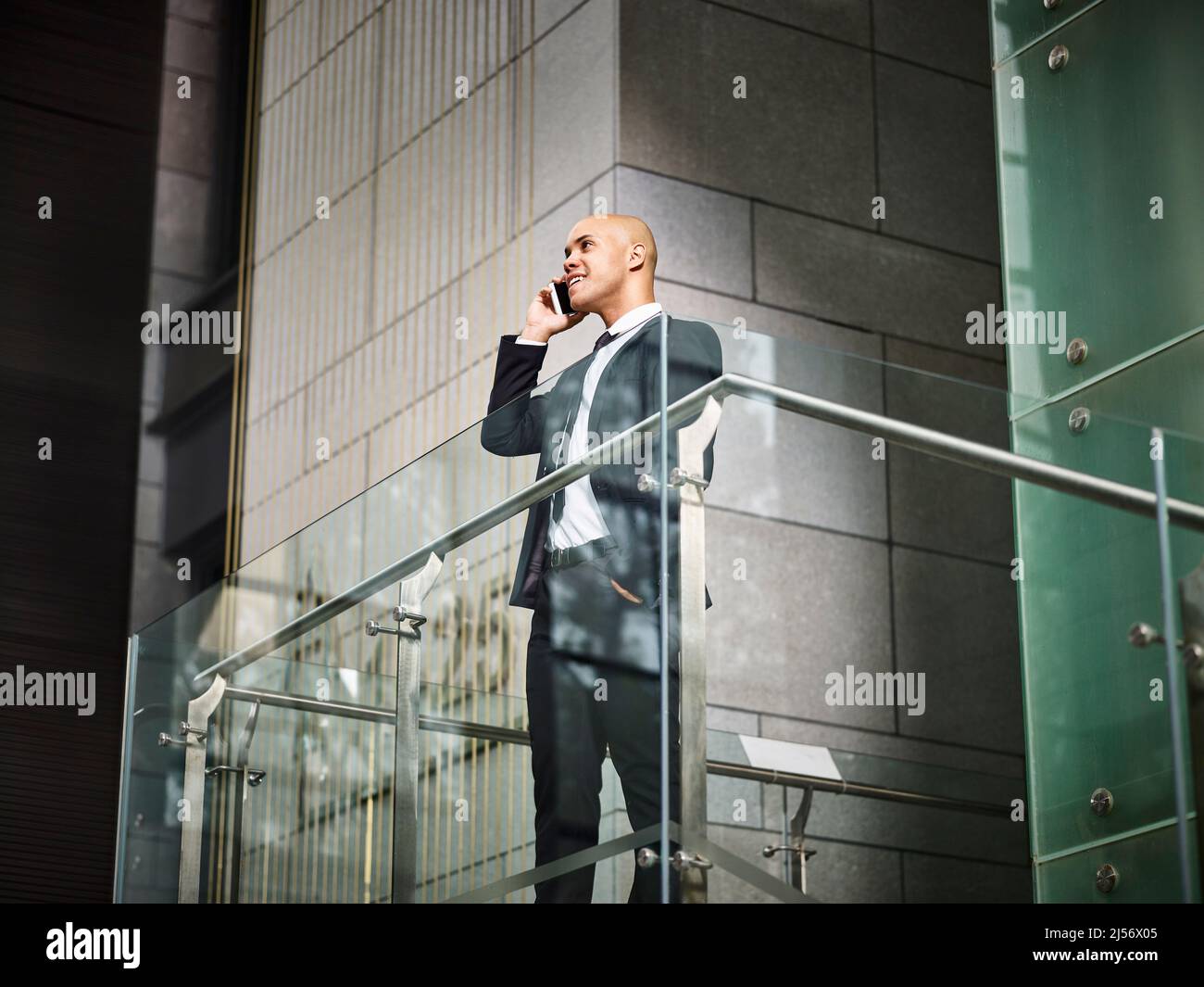 young latino corporate business man standing on top of stairs making a call using cellphone in modern office building Stock Photo