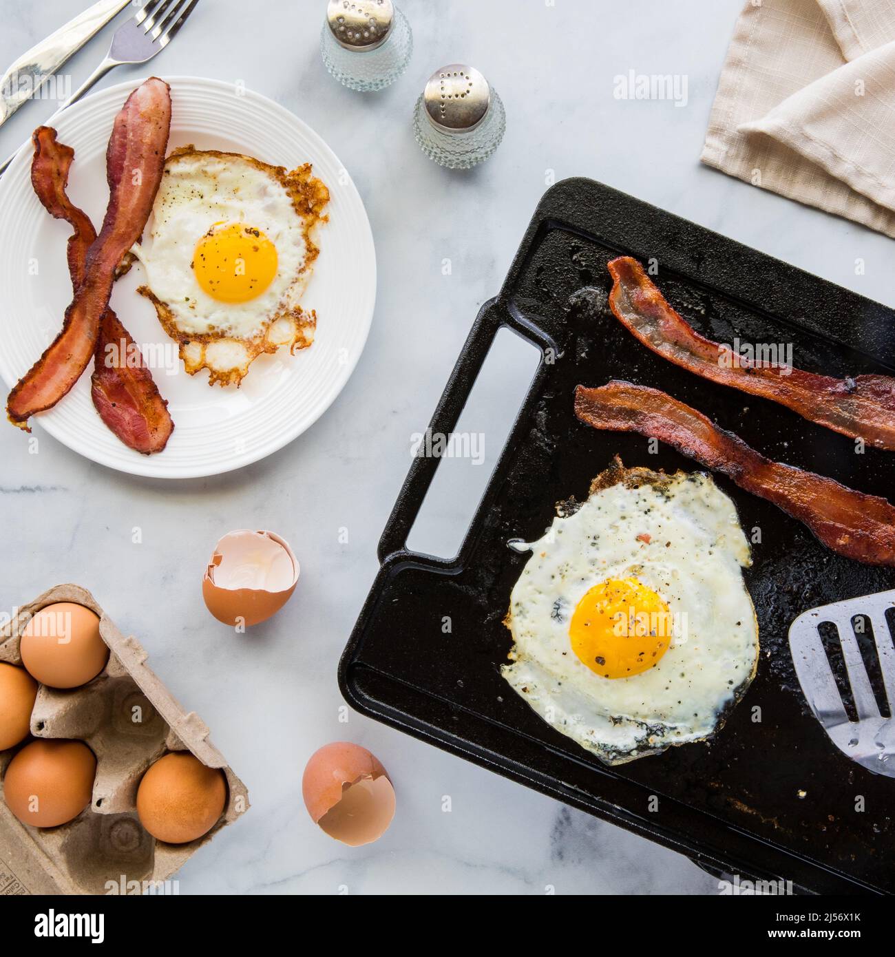 https://c8.alamy.com/comp/2J56X1K/top-down-view-of-a-griddle-pan-cooking-bacon-and-eggs-for-breakfast-2J56X1K.jpg