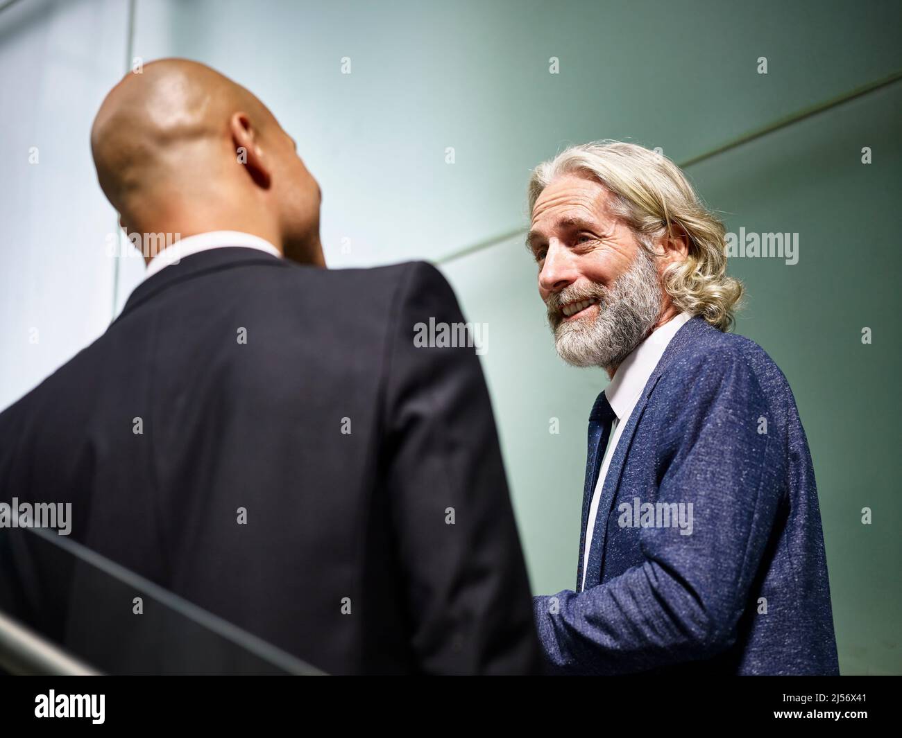 caucasian and latino corporate business men talking chatting having a conversation while walking on stairs in modern office building Stock Photo