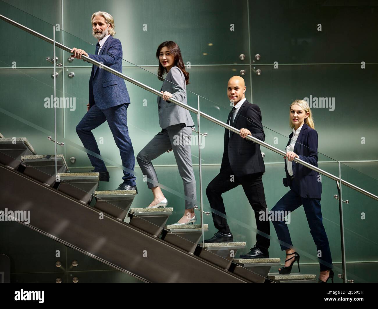 multinational and multiethnic corporate business people male and female walking up stairs in a line looking at camera in modern office building. Stock Photo