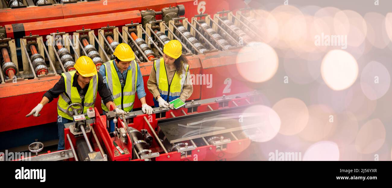 Engineer and operator wearing a safety suit maintaining machine in industrial metal sheet factory, team worker walk teaching help friend operate contr Stock Photo