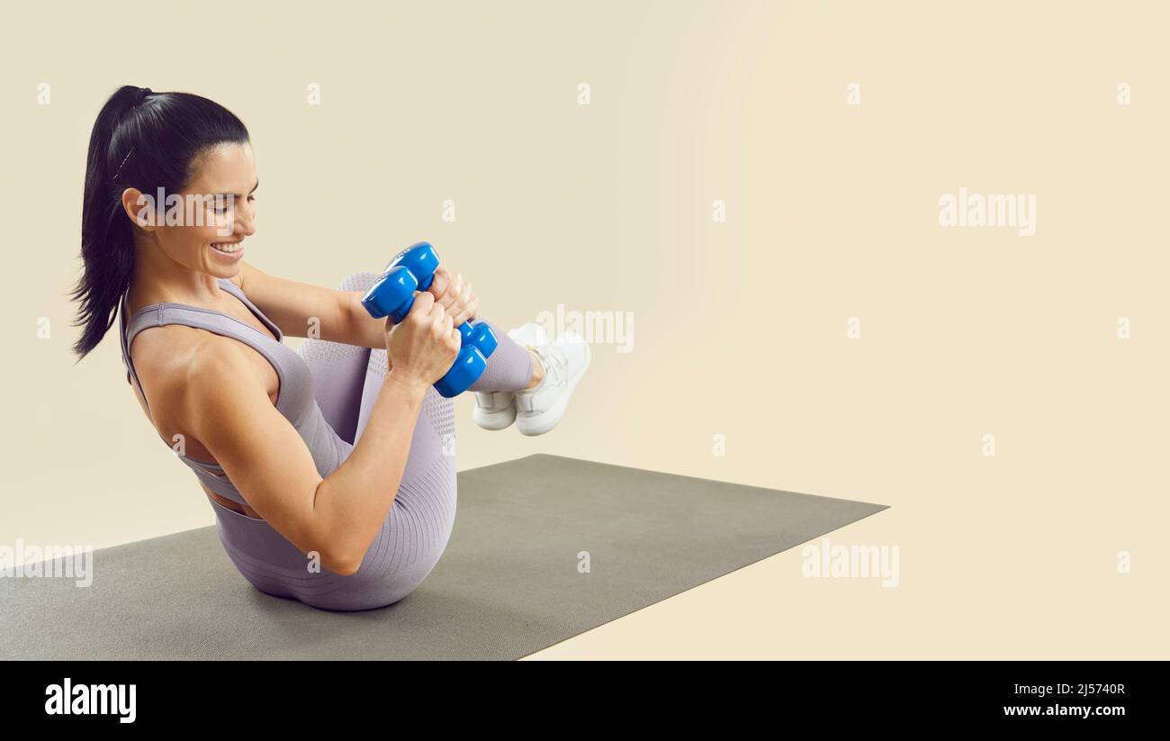 Athletic woman training with dumbbells on fitness mat isolated on light beige background. Stock Photo