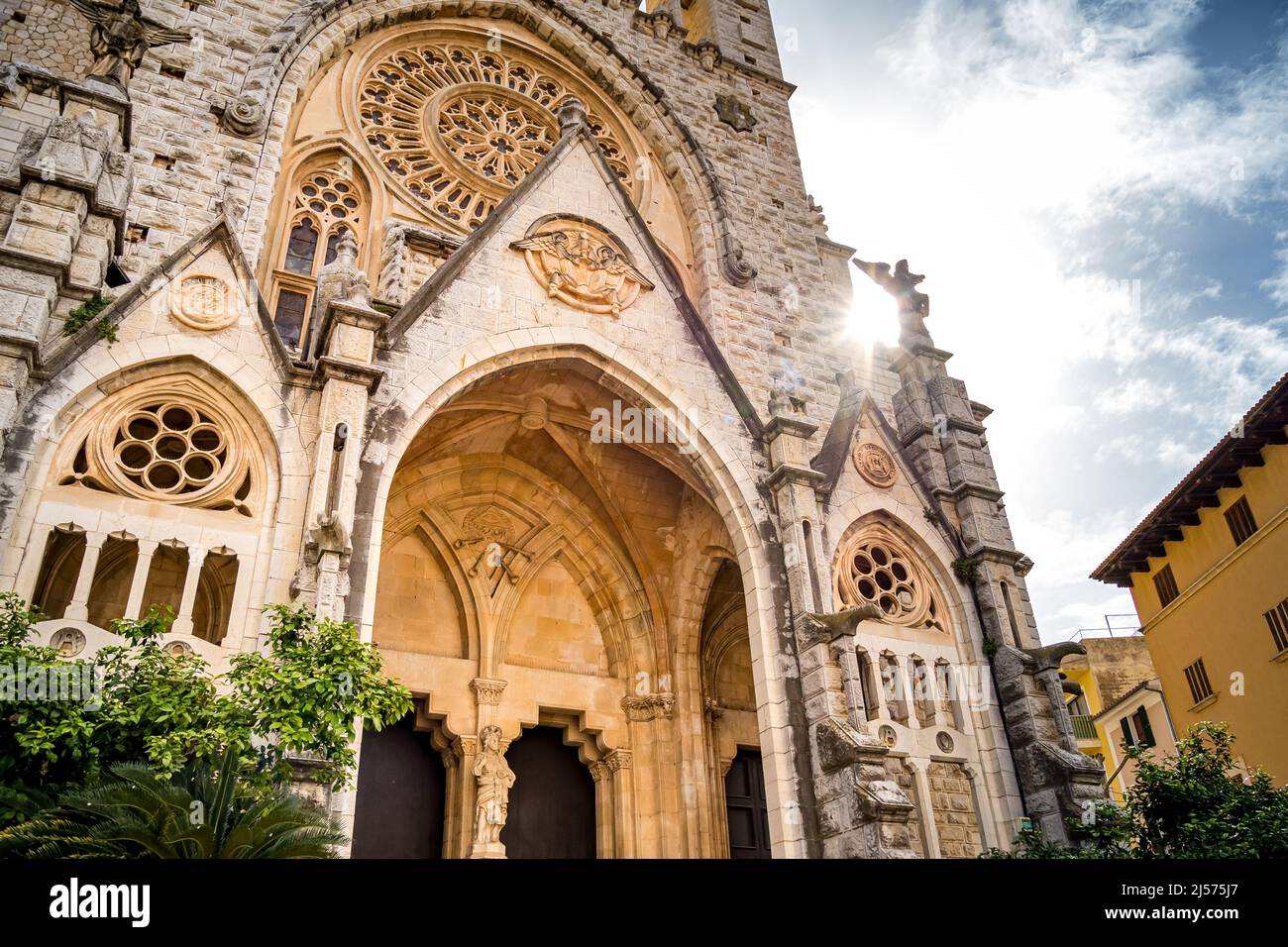 Backlit shot of gothic revival front facade of Sant Bartomeu Church in Soller with rose window ornaments and mighty entry. Popular tourist attraction. Stock Photo