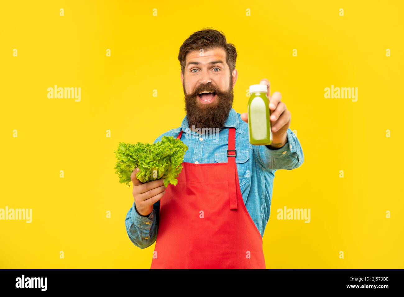 Happy man giving juice bottle holding fresh lettuce yellow background, juice barkeeper Stock Photo