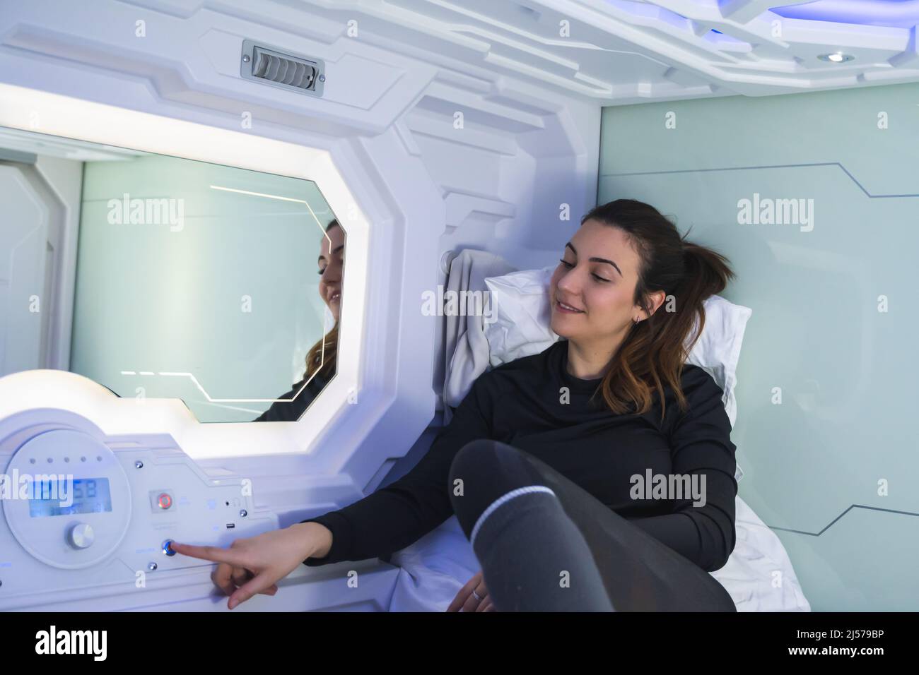 Pretty brunette woman testing the buttons in her capsule bedroom Stock Photo