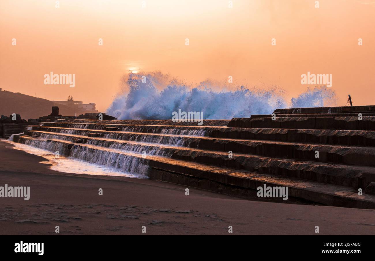 Waves crashing over the steps of the natural sea swimming pool at sunset in Bajamar north Tenerife Canary Islands Stock Photo