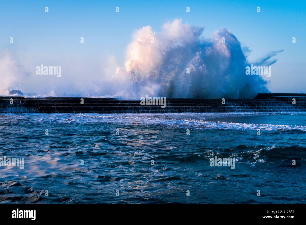 Waves crashing over the steps of the natural sea swimming pool at sunset in Bajamar north Tenerife Canary Islands Stock Photo