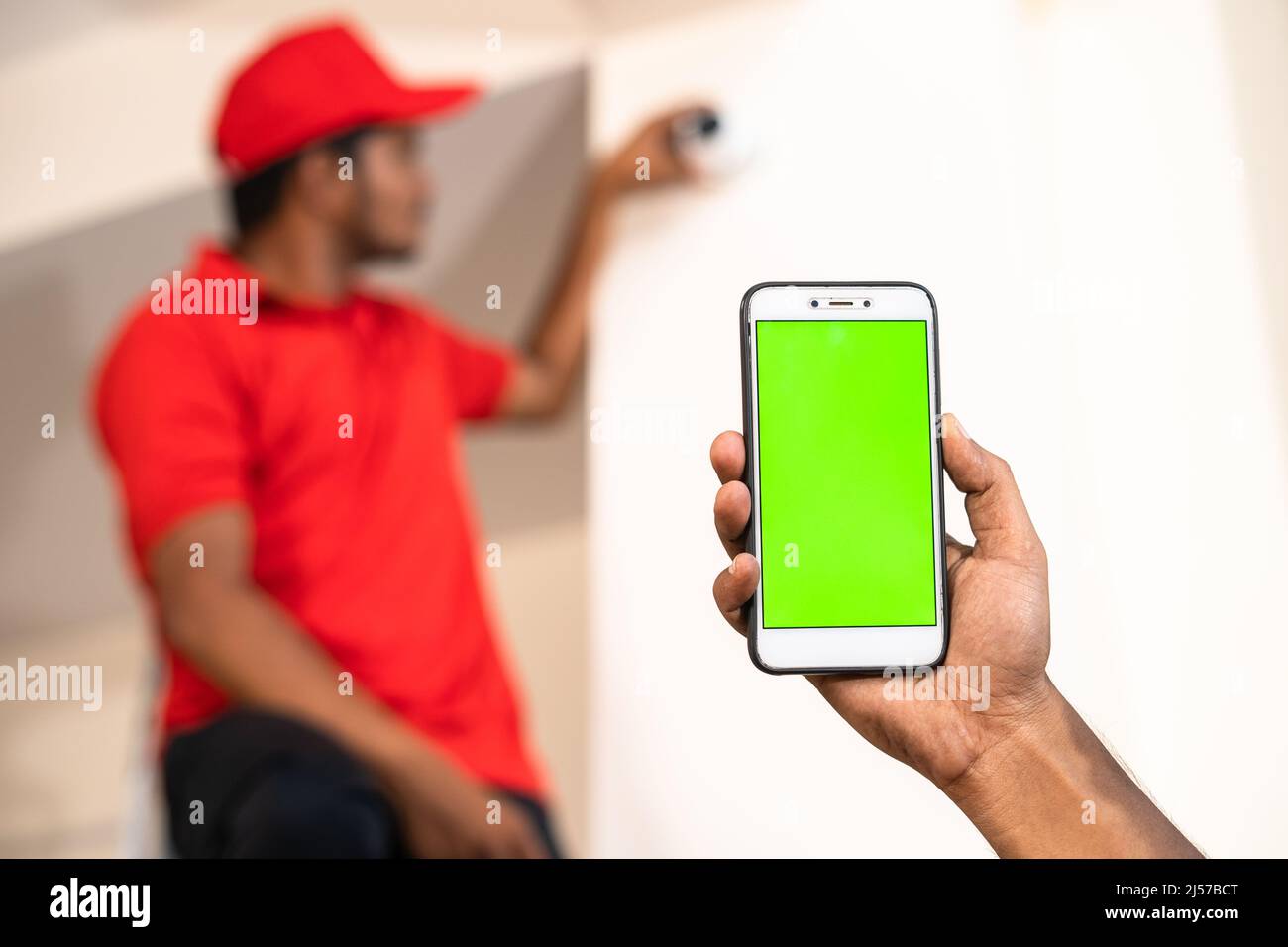 Close up shot of hands showing green screen mobile phone while while electrician fixing cctv camera at home - concept of online booking, advertisement Stock Photo