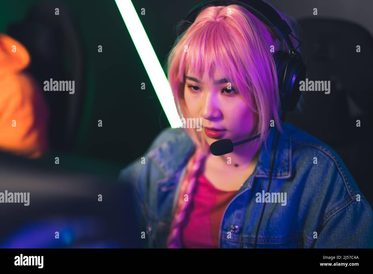 Beautiful concentrated Asian female player in headphones and pink wig playing video games copy space concept medium closeup. High quality photo Stock Photo