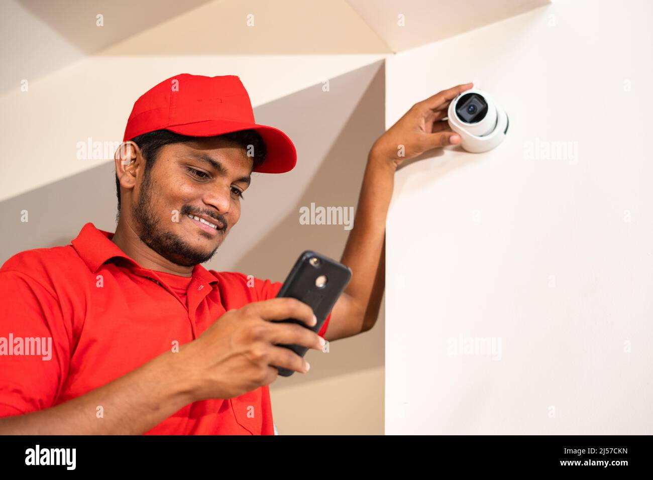 Smiling cctv technician busy using mobile phone for check settings or controlling at home while on ladder - concept of safety, technology and Stock Photo