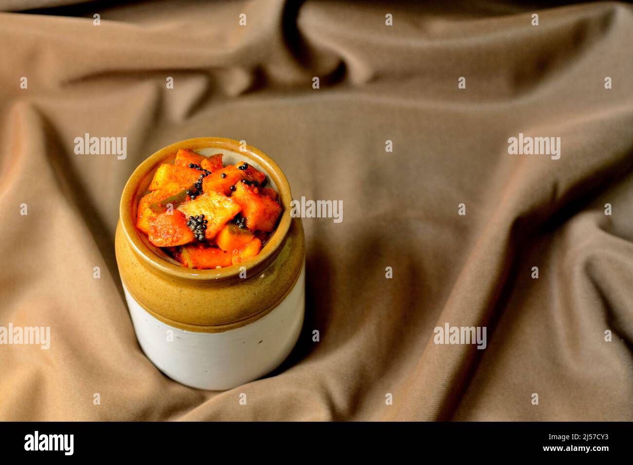 Homemade raw mango pickle in a traditional ceramic jar on Brown background Stock Photo