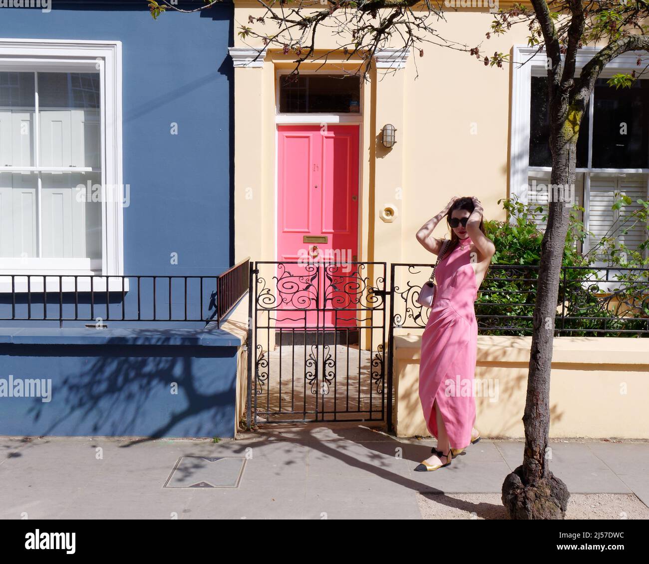 London, Greater London, England, April 09 2022: Woman in pink dress stands in front of a house with a pink door on Portabello Road in Notting Hill. Stock Photo