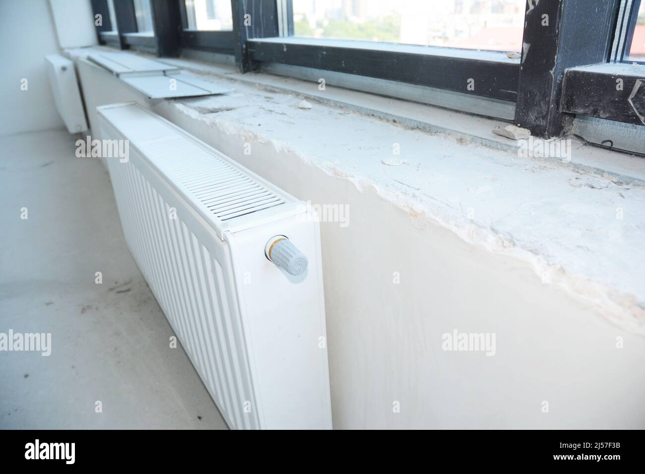 Installing radiator heating with thermostat in the unfinished empty room. Stock Photo