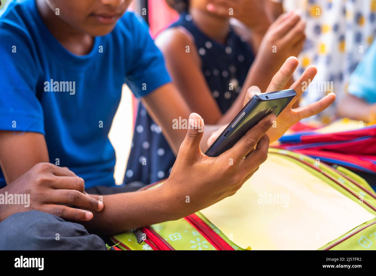 Close up of kids hands busy using mobile phone while sitting at school corridor during break - concept of technology, social media and smartphone Stock Photo