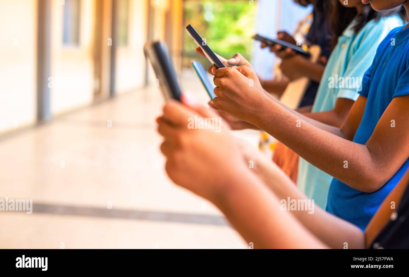 Close up shot, group of children hands busy using smartphone at school corridor - concept of social media, playing games, technology and education Stock Photo
