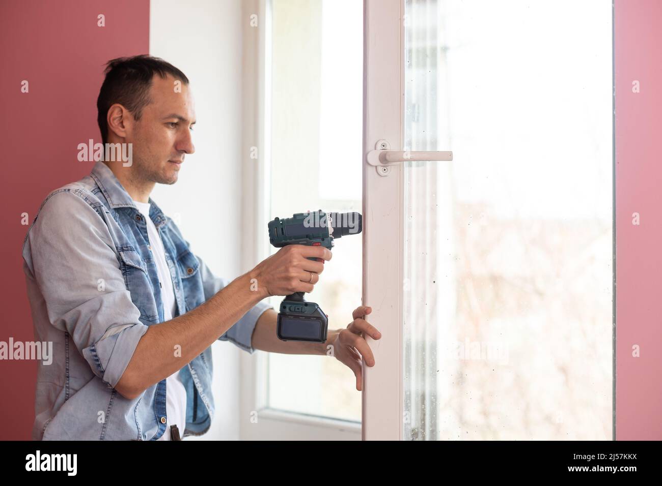 Handyman using a cordless screwdriver to install a window handle. Qualified worker services, home repair and renovation. Stock Photo