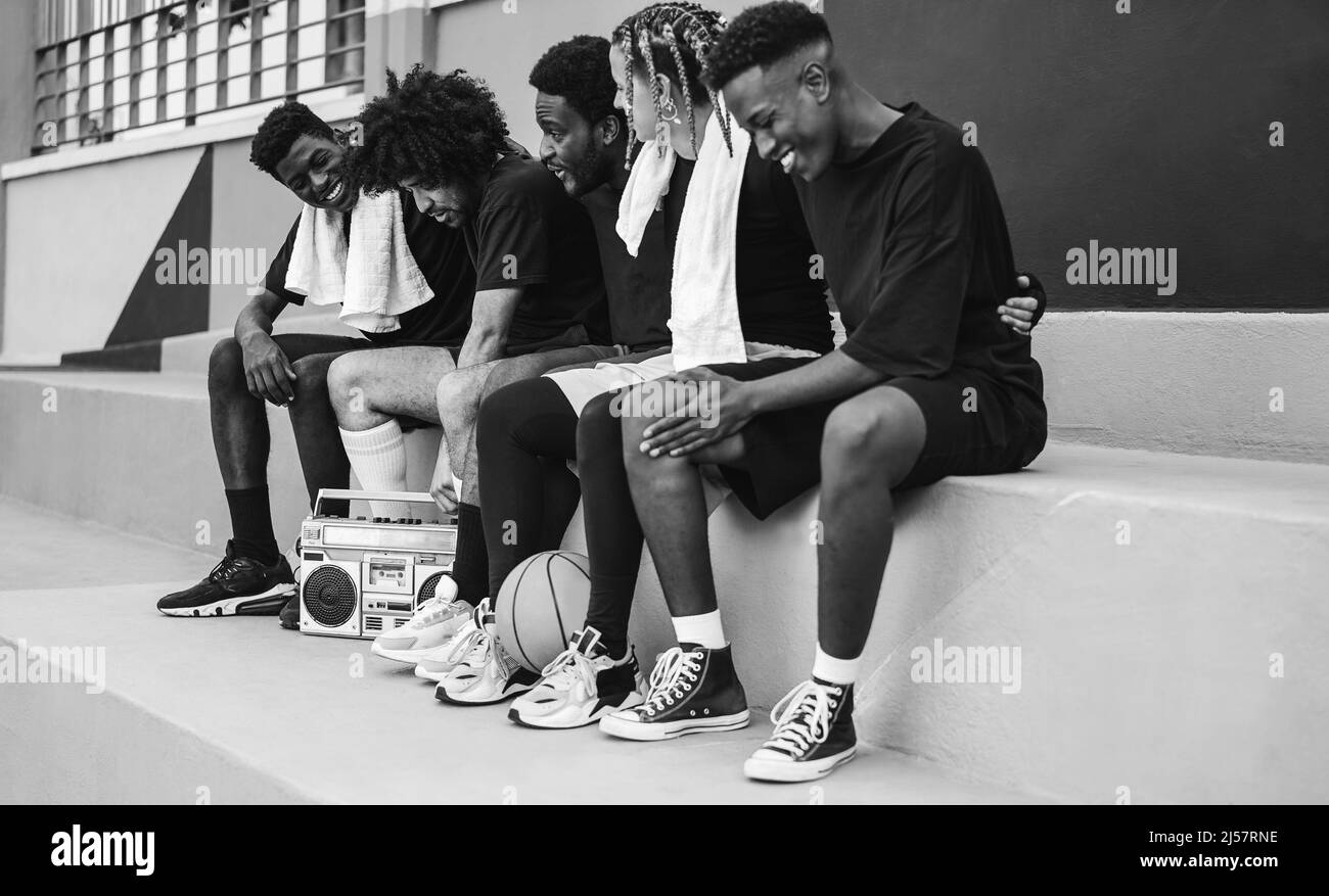 Group of young african people listening music from vintage boombox stereo outdoor after basketball match - Focus on with afro hair - Black and white e Stock Photo