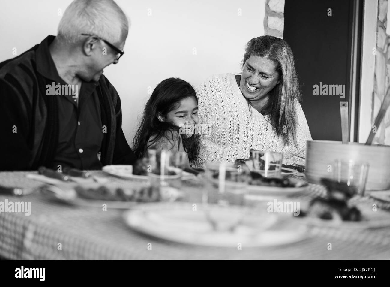 Happy grandparents eating with grand-daughter at home patio - Focus on grandmother face - Black and white editing Stock Photo